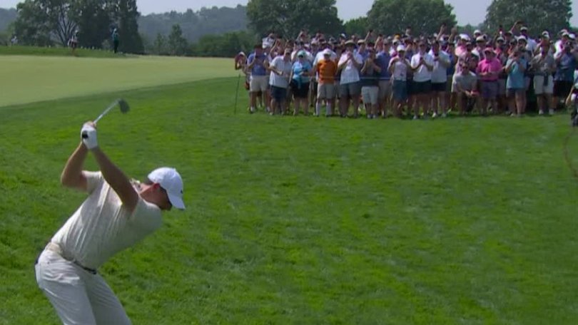 Rory McIlroy hits a shot over a small crowd directly in front of him.