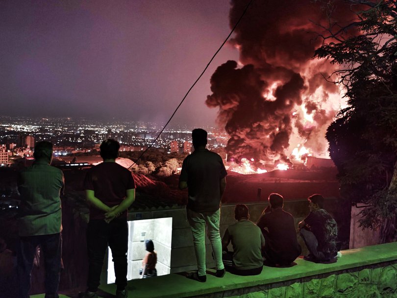 People observe fire and smoke from an Israeli attack on the Shahran oil depot. (Photo by Stringer/Getty Images)