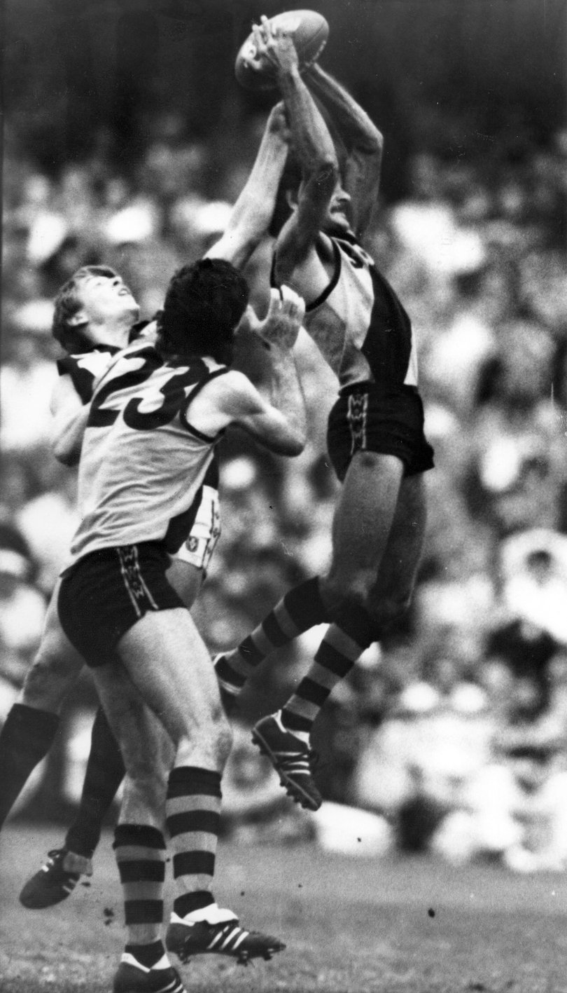 Football State of Origin WA v VIC 1986 - WA rover Michael Mitchell jumps high to grab the ball ahead of Victorian defender Gary Pert. WA centre half forward Peter Sartori is ready to lend a hand. 
(WA winners by 3 points) 
