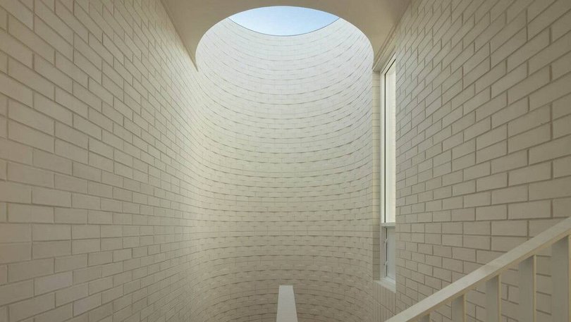 The staircase spirals upwards between rounded white brick walls and a statement circle skylight.