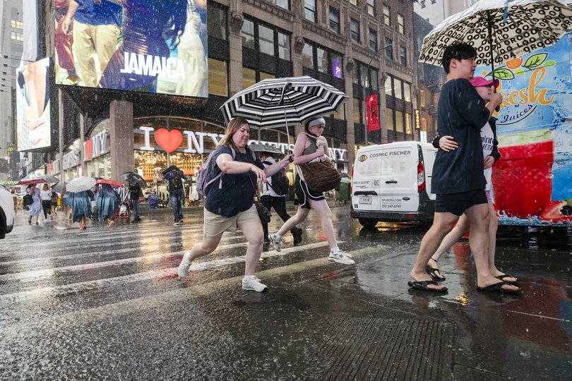 People jump over puddles crossing the street in Times Square during a rainstorm on July 31, 2025 in New York City.
