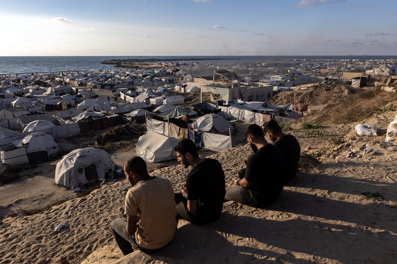 Palestinians sit on a hill looking out over the Mediterranean Sea and a camp for displaced people in Gaza City on June 2, 2025.