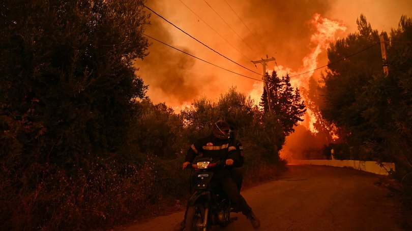 Firefighters leave an area on a scooter as flames approach during a wildfire near the city of Patras, western Greece on August 13, 2025.