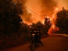 Firefighters leave an area on a scooter as flames approach during a wildfire near the city of Patras, western Greece on August 13, 2025. 