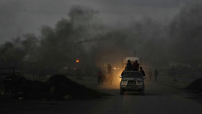 Palestinians ride their vehicles through black smoke along the Sea Road, at dusk in the south of Gaza City ion Thursday.