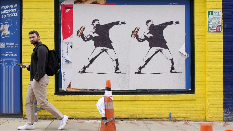 A person walks past Banksy-style posters of a protester throwing a sandwich in Washington, DC.