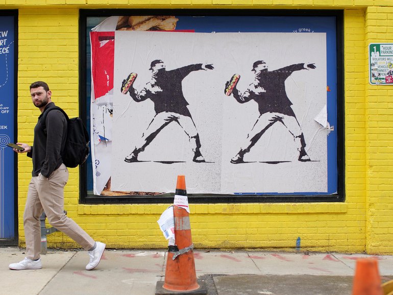 A person walks past Banksy-style posters of a protester throwing a sandwich in Washington, DC. 