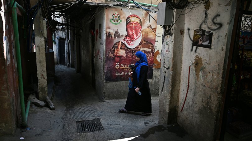 A woman walks past a wall poster depicting Abu Obaida, the spokesman for the Ezzedine al-Qassam Brigades.