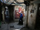 A woman walks past a wall poster depicting Abu Obaida, the spokesman for the Ezzedine al-Qassam Brigades.