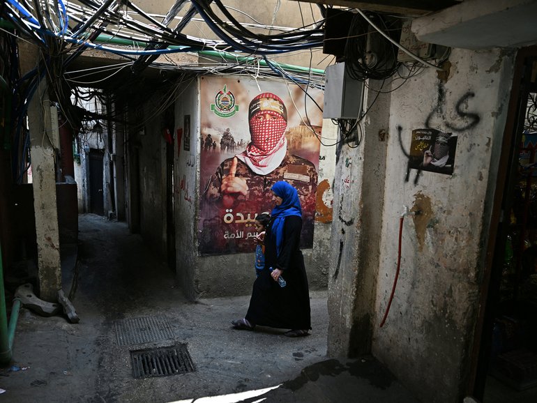 A woman walks past a wall poster depicting Abu Obaida, the spokesman for the Ezzedine al-Qassam Brigades.