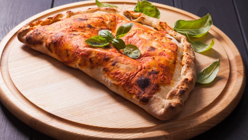 Pizza calzone with basil leaves close up 