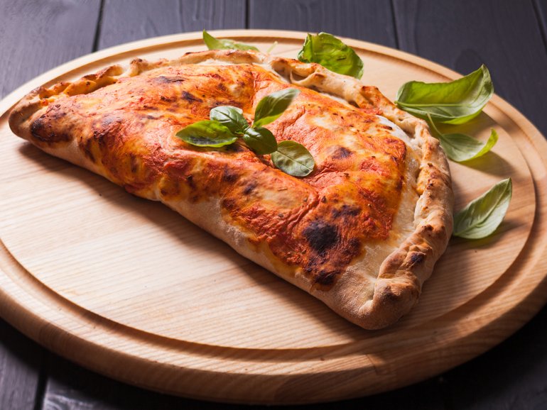 Pizza calzone with basil leaves close up 