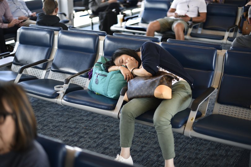 An airplane passenger waiting for her flight sleeps in the terminal gate.
