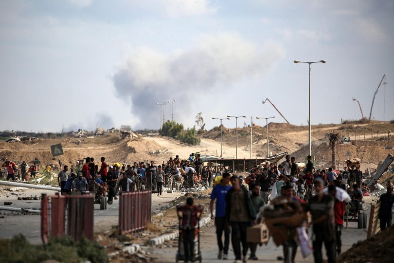 A plume of smoke rises in the background as Palestinians return from a food distribution point run by the US and Israeli-backed Gaza Humanitarian Foundation (GHF) group, near the Netsarim corridor in the central Gaza Strip on October 5, 2025. 