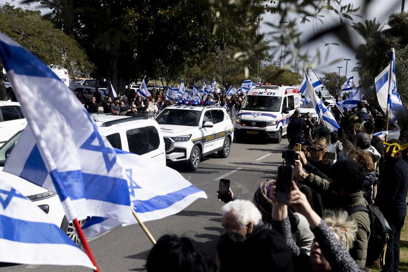 FILE: People stand with flags as a convoy transporting four released bodies of hostages arrives in Israel.