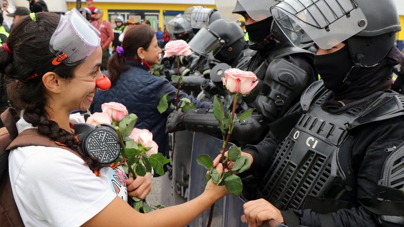 A protester wearing a clown nose hands roses to riot police before a march against racism, the criminalization of protest, and in support of the national strike called by CONAIE in Quito.
