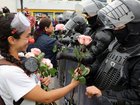 A protester wearing a clown nose hands roses to riot police before a march against racism, the criminalization of protest, and in support of the national strike called by CONAIE in Quito.