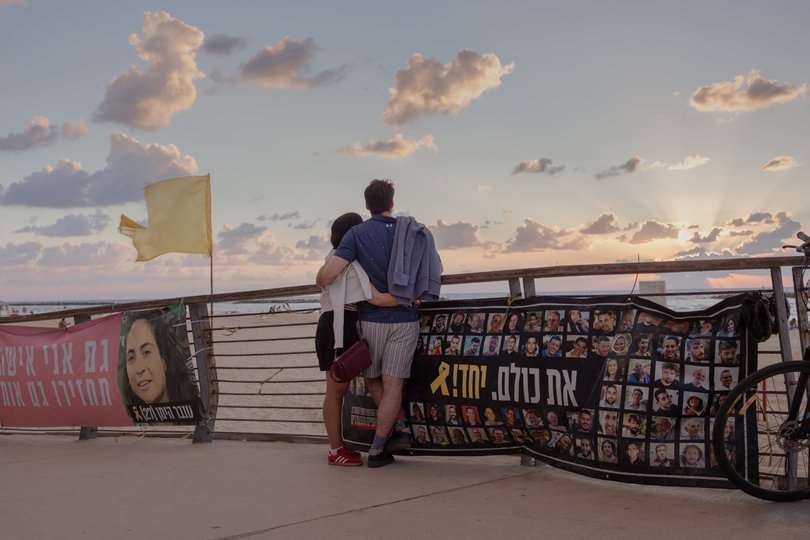 Surrounded by banners about hostages held by Hamas, a couple enjoys sunset over the Mediterranean Sea in Tel Aviv.