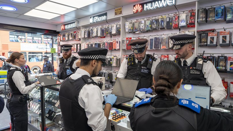 Police officers search a second-hand phone shop in London, September 25, 2025.