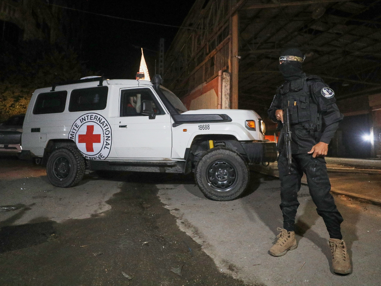A Hamas gunman stands guard as Red Cross vehicles allegedly transporting coffins containing the bodies of four deceased hostages leave a warehouse for Israel.
