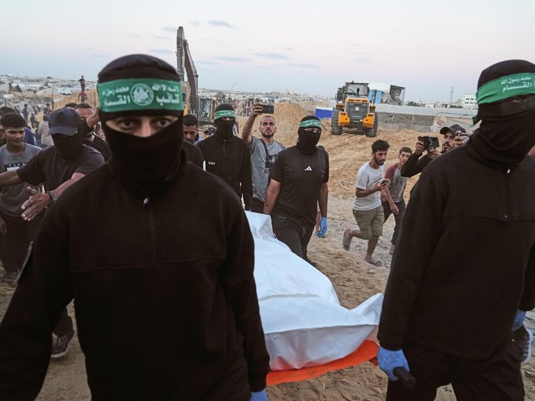 Hamas militants carry a white bag believed to contain a body, during a search for the remains of hostages in Hamad City, Khan Younis, in southern Gaza, on Tuesday, October 28, 2025. 