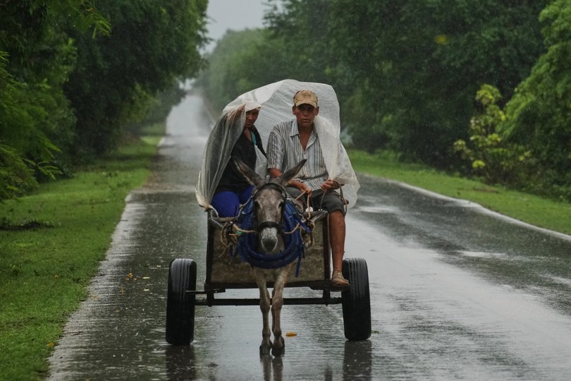 A couple rides under plastic on a donkey-pulled cart in the rain before the arrival of Hurricane Melissa in Canizo, a vilage in Santiago de Cuba, Tuesday, Oct. 28, 2025. (AP Photo/Ramón Espinosa)