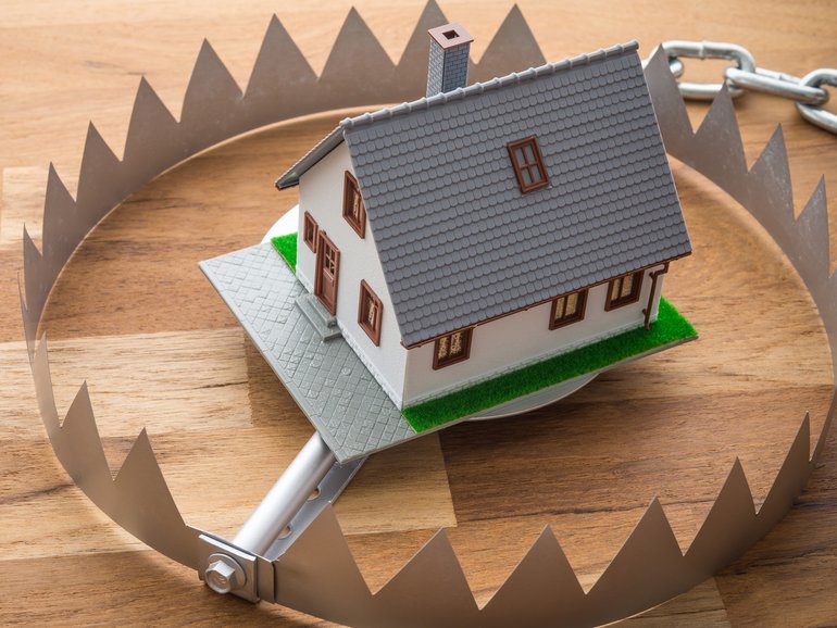 Mortgage house in a trap on wooden table background. House trap on debt or loan problem or risk in real estate property financing concept.