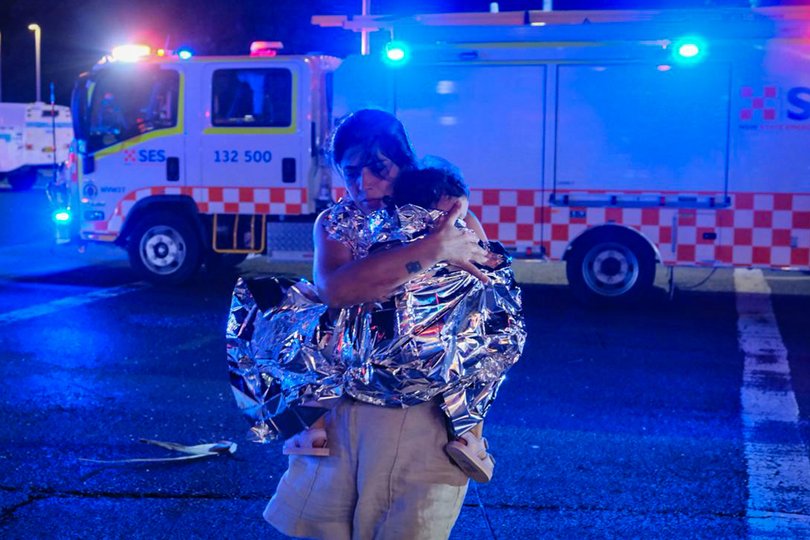 A member of the public leaves the scene with her child, who is covered in an emergency blanket, after a shooting at Bondi Beach.