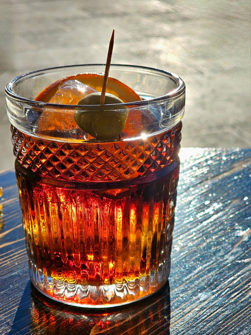 A glass of vermut with orange and olive.
