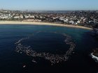 Members of the Bondi community paddle and swim into the ocean and form a circle to pay respect during a Paddle Out to honour victims.