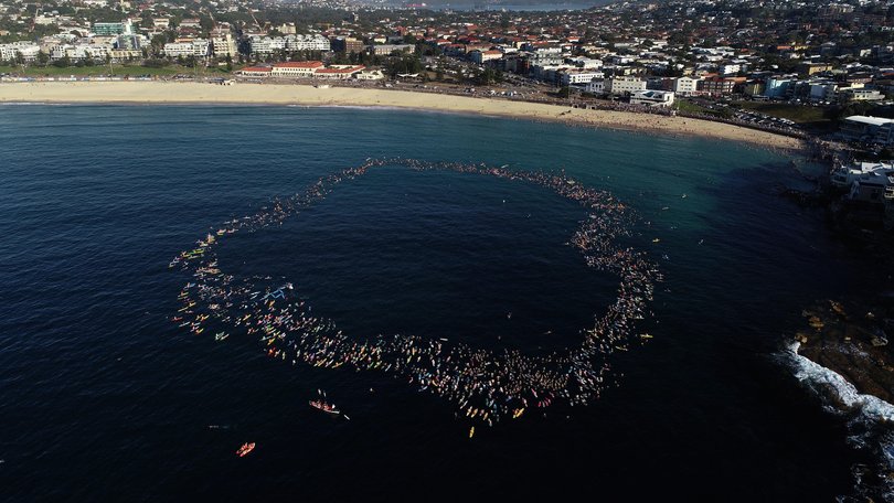 Members of the Bondi community paddle and swim into the ocean and form a circle to pay their respects.