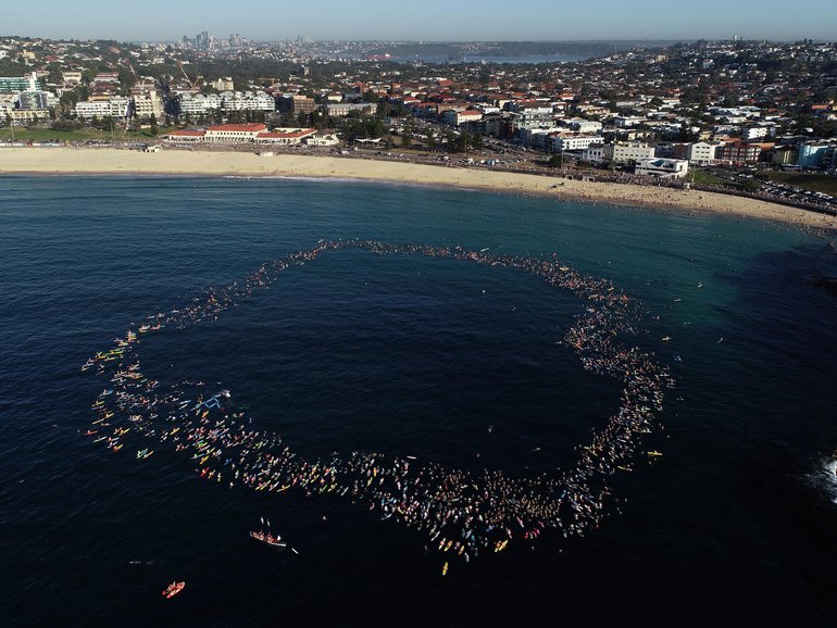 Members of the Bondi community paddle and swim into the ocean and form a circle to pay their respects.