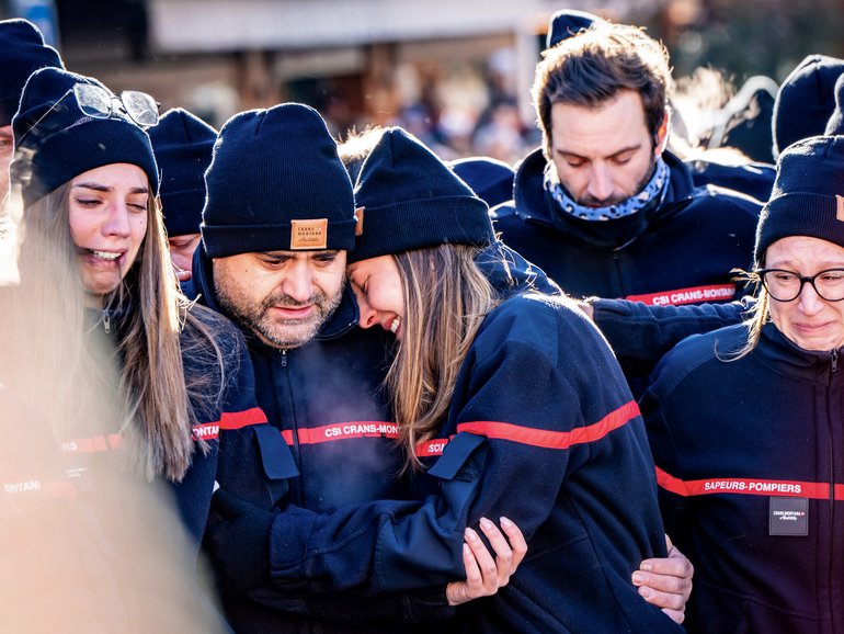 Firefighters from the Municipality of Crans-Montana react as they gather around a makeshift memorial to pay their respects by laying flowers, candles and messages near the Constellation bar, on January 4, 2026, in Crans-Montana in honour of the victims of the fire that ripped through the venue in the luxury Alpine ski resort on New Year's Eve. Authorities investigating the New Year's blaze in the Swiss resort of Crans-Montana have identified 24 of the 40 people killed, including 11 minors and six foreign nationals, police said on January 4, 2026. Also 119 were injured during the fire, most of them seriously, according to the latest toll. (Photo by MAXIME SCHMID / AFP)