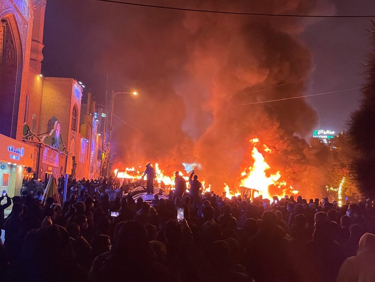 Iranian protesters gather around burning cars near a masque while blocking a street during a protest in Tehran.