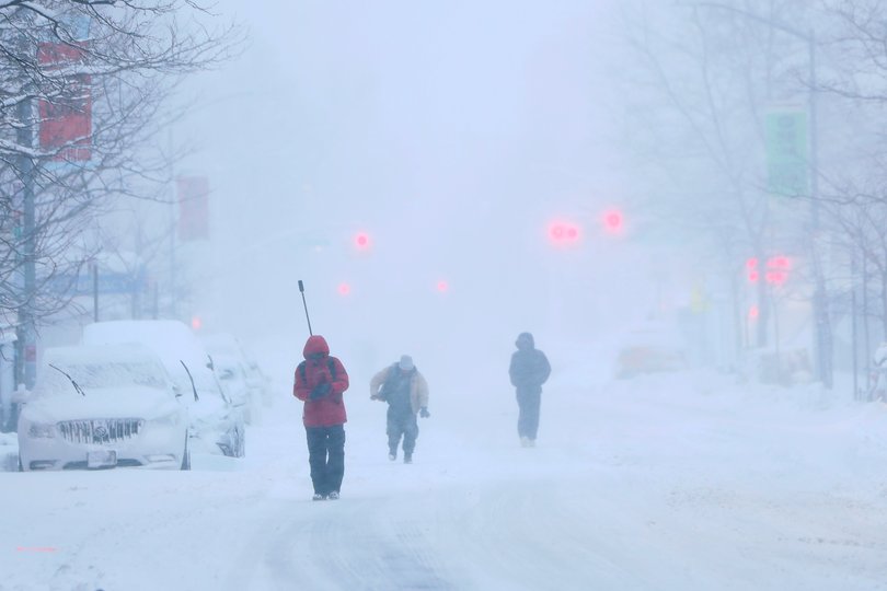 People walk along snow covered streets as snow falls during a blizzard on February 23, 2026 in the Flatbush neighborhood of the Brooklyn borough in New York City. 