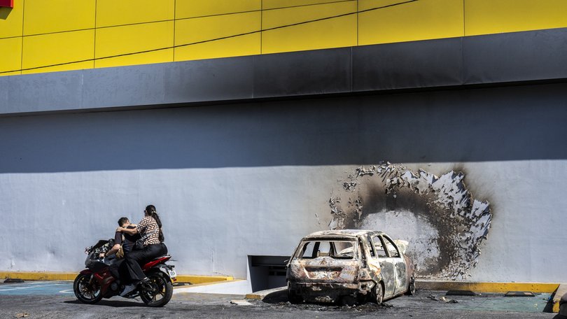 A burned car sits beside a damaged business, one day after the Mexican military killed Nemesio Oseguera Cervantes.
