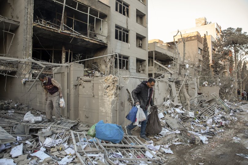 People remove their belongings from a damaged residential building after a police station was struck by airstrikes in Tehran, Iran.