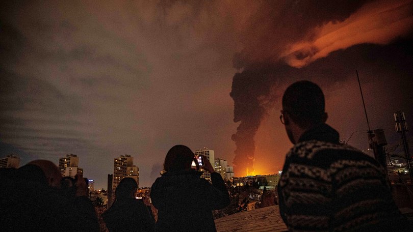 Residents look on as flames and smoke rise from an oil storage facility struck in the US–Israeli attacks.