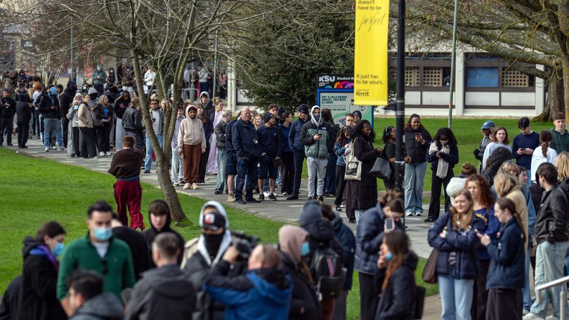 Staff and students, some wearing face masks, queue at the University of Kent in Canterbury after an outbreak of meningitis caused the deaths of two people.