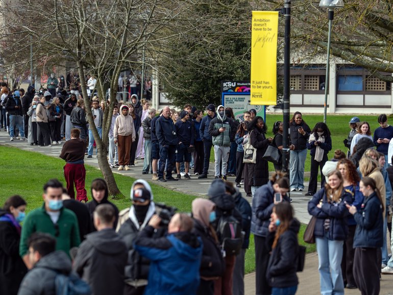 Staff and students, some wearing face masks, queue at the University of Kent in Canterbury after an outbreak of meningitis caused the deaths of two people.