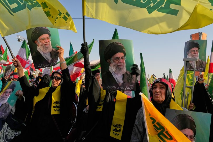 Hezbollah supporters hold photos of late Iranian Supreme Leader Ayatollah Ali Khamenei while wrapped in Hezbollah and Iran flags.