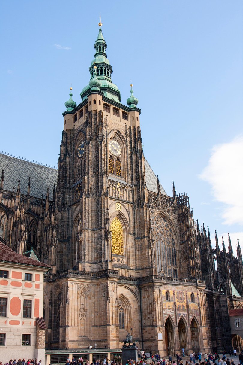 Front view of the main entrance to the St. Vitus cathedral. Tourists and locals are walking on Hradčany Castle Square. 
