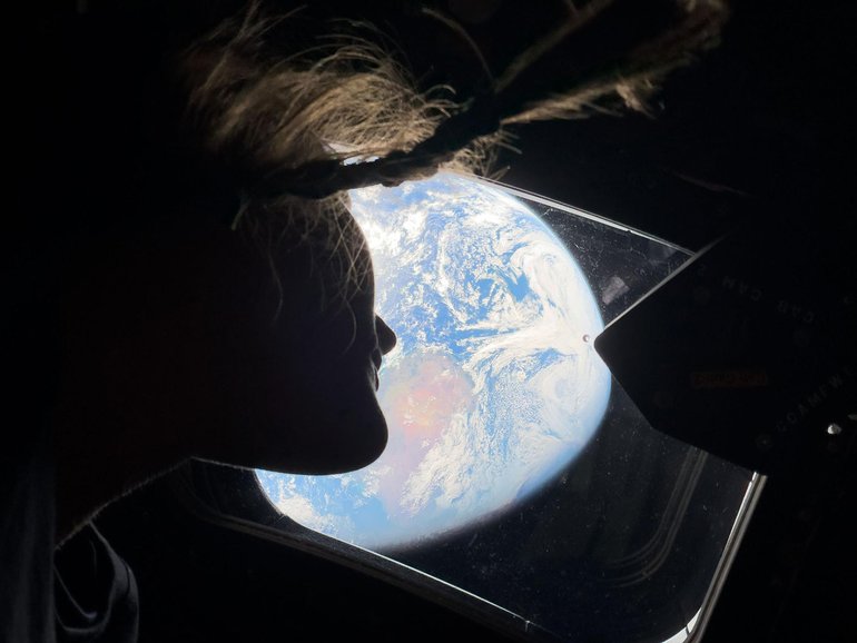 A photo provided by NASA shows NASA astronaut and Artemis II mission specialist Christina Koch as she peers out of one of the Orion spacecraft's main cabin windows, looking back at Earth, as the crew travels towards the Moon, April 4, 2026. The astronauts said they had lost track of which day it is on Earth on their transit to the moon. (NASA via The New York Times) — NO SALES; EDITORIAL USE ONLY—