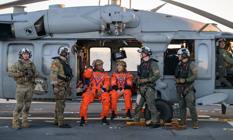 NASA astronaut Victor Glover, Artemis II pilot, left, and NASA astronaut Christina Koch, Artemis II mission specialist are seen sitting on a Navy MH-60 Seahawk from Helicopter Sea Combat Squadron (HSC) 23 on the flight deck of USS John P. Murtha.