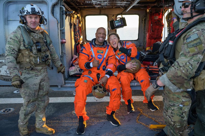 NASA astronaut Victor Glover, Artemis II pilot, left, and NASA astronaut Christina Koch, Artemis II mission specialist are seen sitting on a Navy MH-60 Seahawk from Helicopter Sea Combat Squadron (HSC) 23 on the flight deck of USS John P. Murtha.