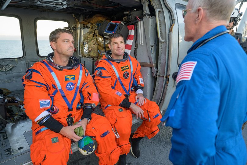 NASA astronaut Victor Glover, Artemis II pilot, left, and CSA (Canadian Space Agency) astronaut Jeremy Hansen, Artemis II mission specialist, talk with NASA Flight Surgeon Richard Scheuring at their Navy MH-60 Seahawk from Helicopter Sea Combat Squadron (HSC) 23 on the flight deck of USS John P. Murtha.