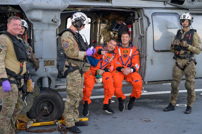 NASA astronaut Reid Wiseman, Artemis II commander, left, and CSA (Canadian Space Agency) astronaut Jeremy Hansen, Artemis II mission specialist, are seen sitting on a Navy MH-60 Seahawk from Helicopter Sea Combat Squadron (HSC) 23 on the flight deck of USS John P. Murtha.