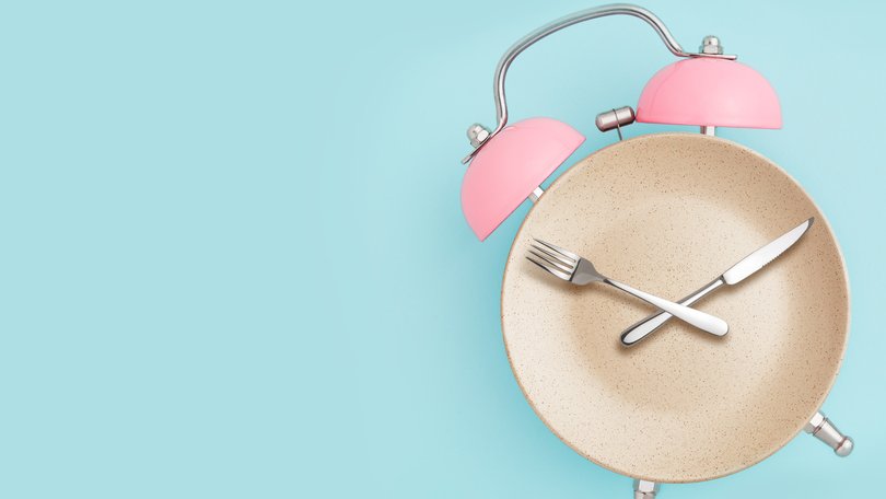 Alarm clock and plate with cutlery . Concept of intermittent fasting, lunchtime, diet and weight loss 