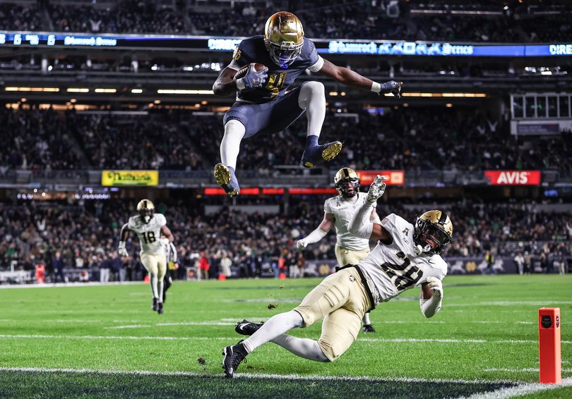 Jeremiyah Love #4 of the Notre Dame Fighting Irish hurdles over Donavon Platt #28 of the Army Black Knights to score a touchdown
