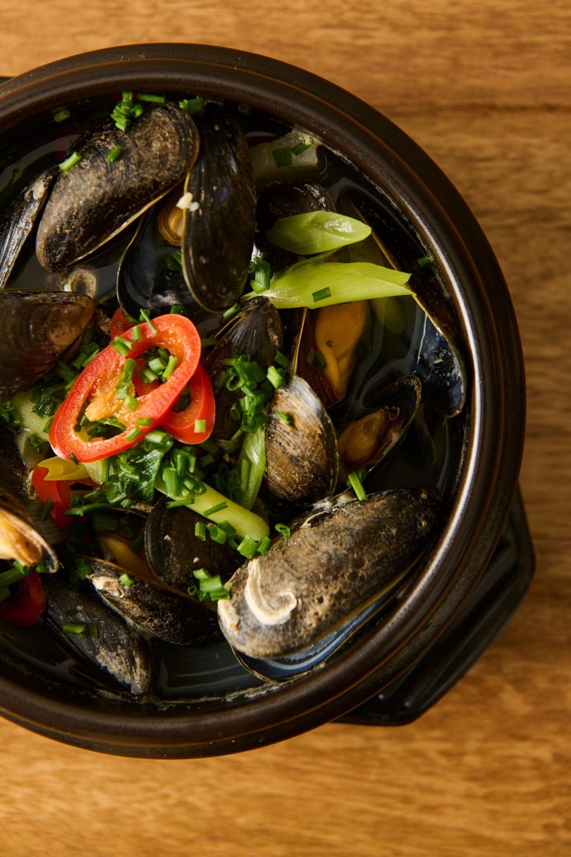In a white-lit, minimalistic room with wooden tables and clay pots, friendly waiters guide diners through a small menu centred on sharing dishes.